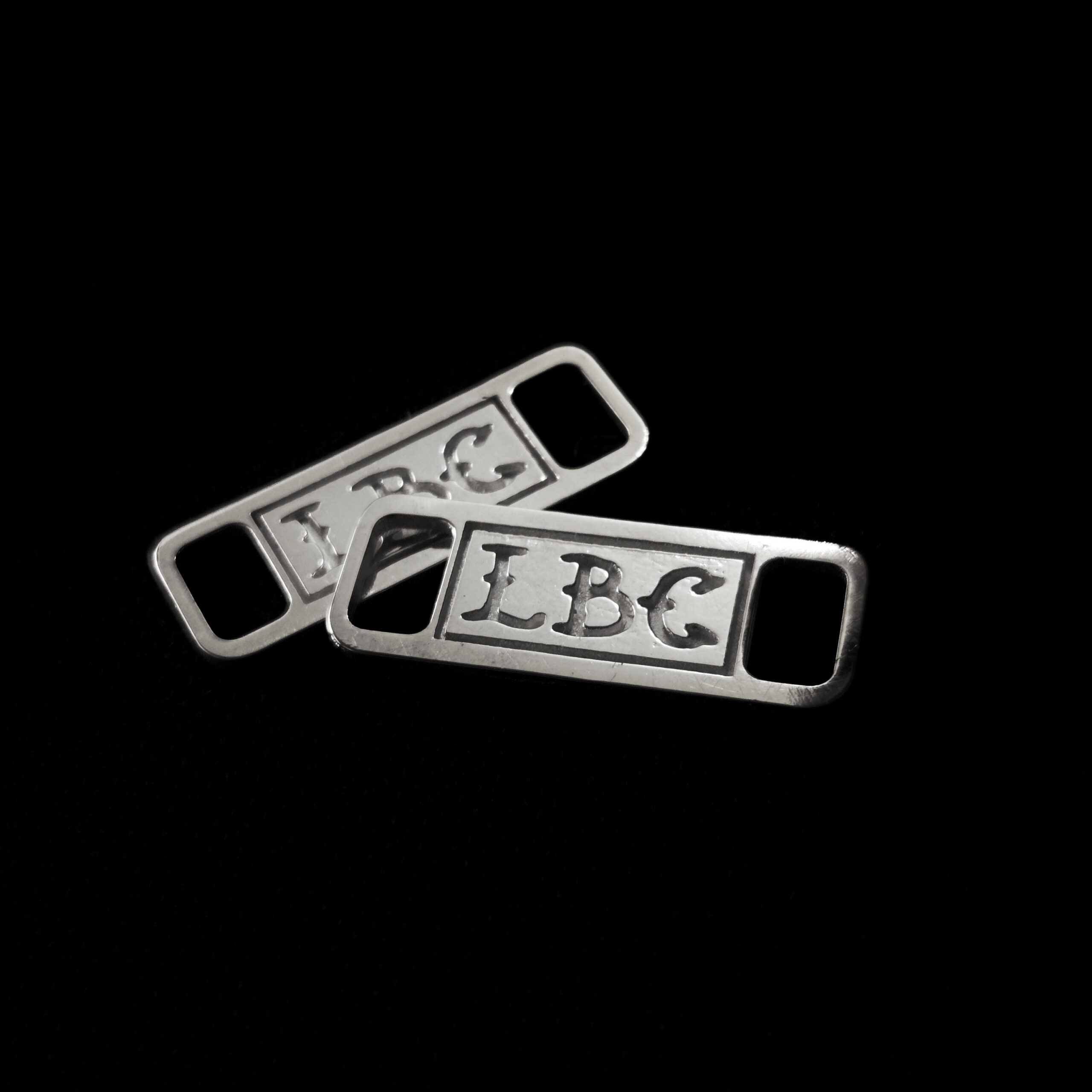 Image of two 925 silver shoelace charms that spell "LBC" on both separately.
